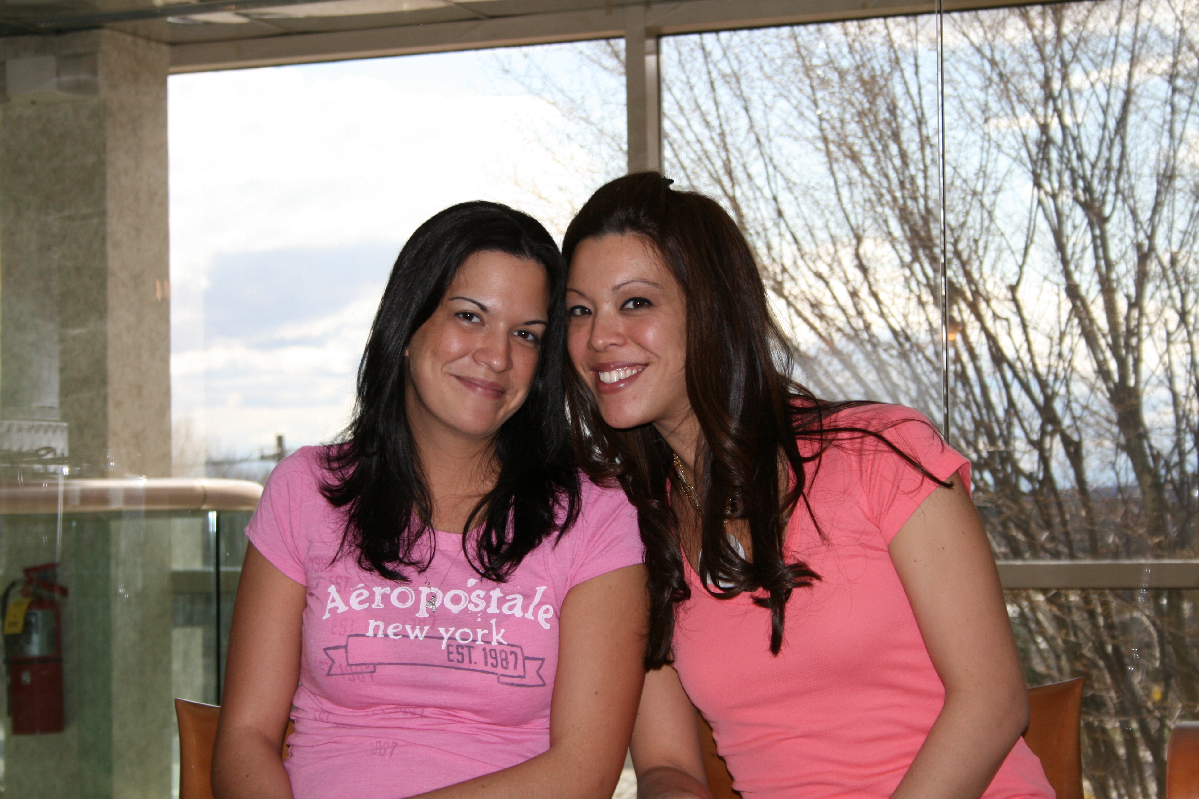 A picture of two sisters with brunette hair sitting in front of a window.